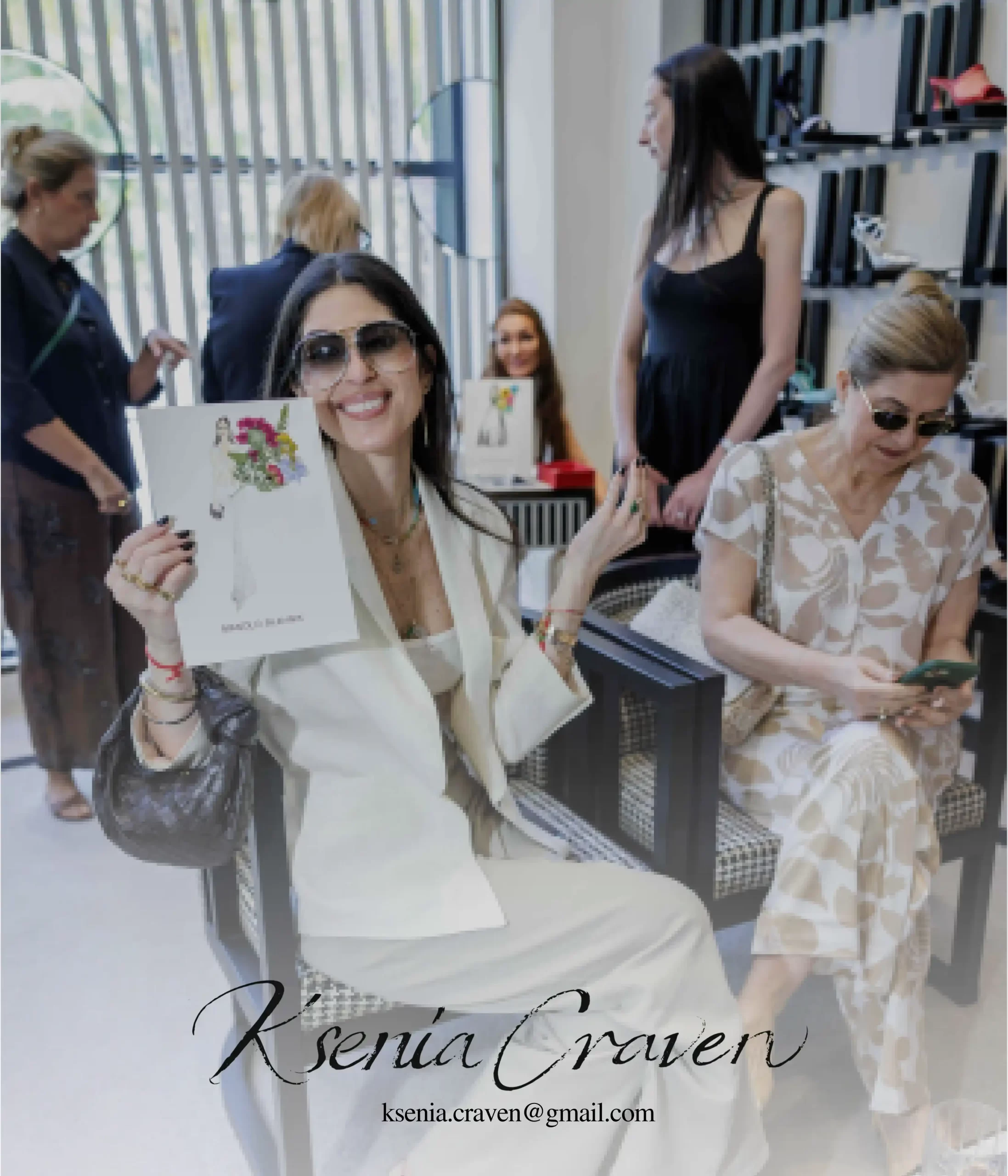 A smiling woman in a white suit holding a custom fashion illustration by Ksenia Craven at a luxury boutique.