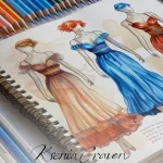 Three hand-drawn fashion sketches in a sketchbook with colored pencils, featuring elegant evening gowns and dresses.