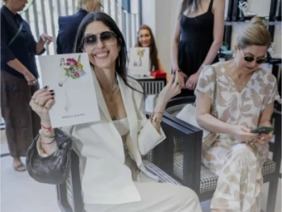 A smiling woman in a white suit holding a custom fashion illustration by Ksenia Craven at a luxury boutique.