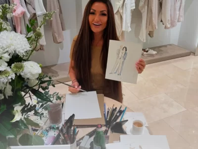 Fashion illustrator Ksenia Craven holding a hand-drawn sketch of a couple in a luxury retail setting.